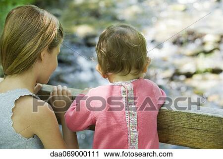Stock Image - Girl and baby sister looking over railing, rear view. Fotosearch