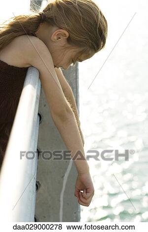 Stock Photo - Girl hanging over side of pier, looking down at water, side view. Fotosearch