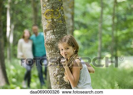Girl hiding behind tree with finger on lips View Large Photo Image Stock Photograph - Girl hiding behind tree with finger on lips. Fotosearch