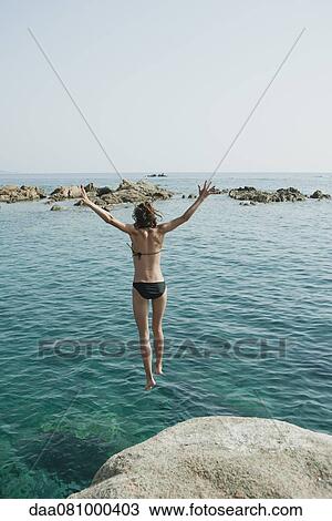 Stock Image - Girl in bikini jumping into ocean, rear view. Fotosearch