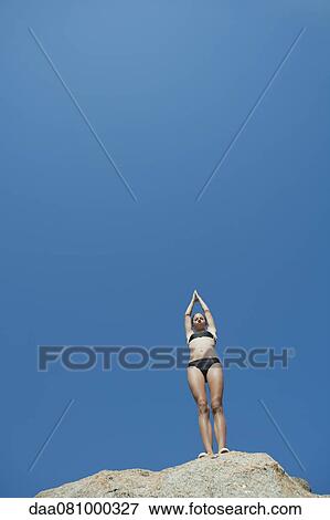 Stock Photo - Girl in bikini standing against blue sky preparing to dive. Fotosearch