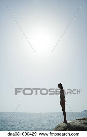 Girl in bikini standing on edge of cliff looking at ocean View Large Photo Image Stock Photo - Girl in bikini standing on edge of cliff looking at ocean. Fotosearch