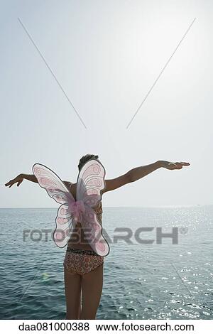 Girl in bikini wearing butterfly costume, standing by ocean with arms outstretched View Large Photo Image Stock Photo - Girl in bikini wearing butterfly costume, standing by ocean with arms outstretched. Fotosearch