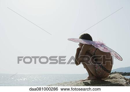 Girl in bikini wearing butterfly costume, crouching on rock and looking at ocean View Large Photo Image Stock Photograph - Girl in bikini wearing butterfly costume, crouching on rock and looking at ocean. Fotosearch