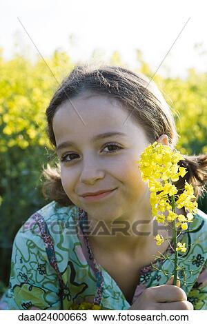 Girl in field of yellow flowers, holding up blossom, portrait View Large Photo Image Stock Image - Girl in field of yellow flowers, holding up blossom, portrait. Fotosearch