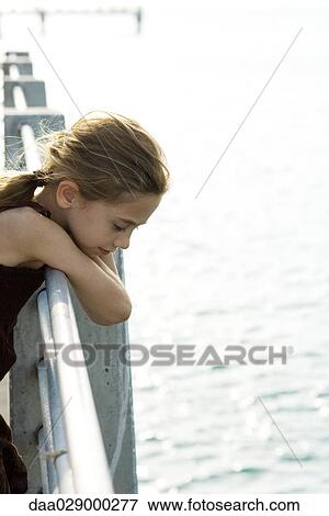 Girl leaning over railing on pier, looking down at water, side view View Large Photo Image Stock Photo - Girl leaning over railing on pier, looking down at water, side view. Fotosearch