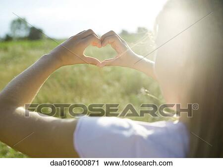 Stock Image - Girl making heart shape with hands, over the shoulder view. Fotosearch