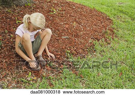 Stock Photo - Girl sitting on the ground, looking down at feet. Fotosearch