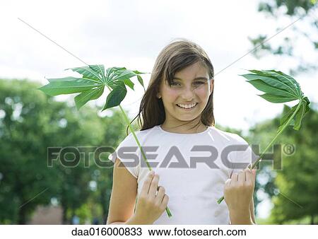 Stock Image - Girl standing holding cassava leaves. Fotosearch