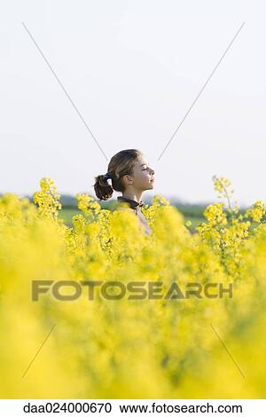 Stock Image - Girl standing in field of canola in bloom, side view, selective focus. Fotosearch