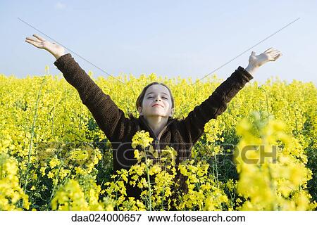 Stock Photo - Girl standing in field of canola in bloom, head back, eyes closed and arms raised. Fotosearch