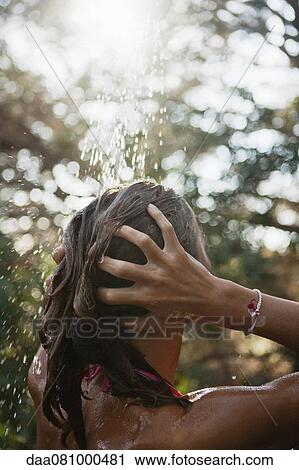 Stock Image - Girl washing hair under running water outdoors, rear view. Fotosearch