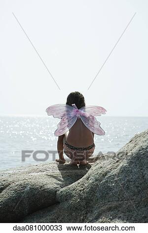 Girl wearing butterfly costume, crouching on rock and looking at ocean View Large Photo Image Stock Image - Girl wearing butterfly costume, crouching on rock and looking at ocean. Fotosearch