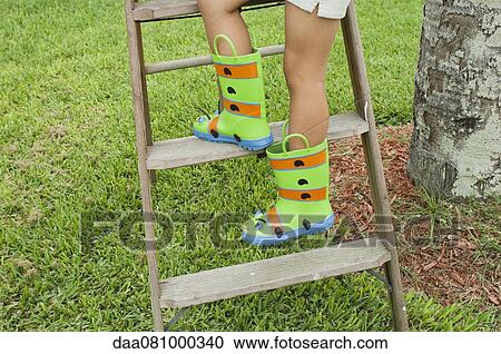 Stock Image - Girl wearing rubber boots, climbing ladder, cropped. Fotosearch