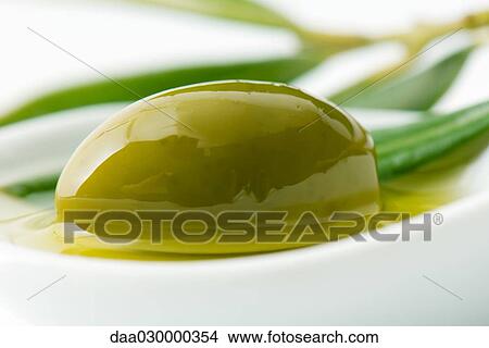 Picture - Green olive and oil in dish, close-up. Fotosearch