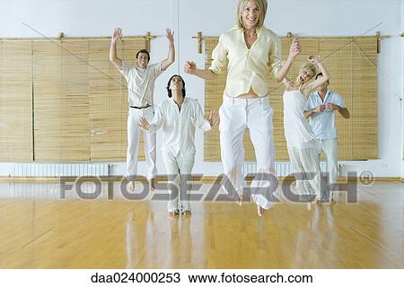 Stock Image - Group of adults in wellness center jumping into air. Fotosearch