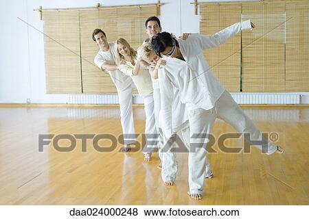 Stock Photo - Group of adults standing single file holding onto each others' shoulders, blindfolded leader lifting one leg up. Fotosearch