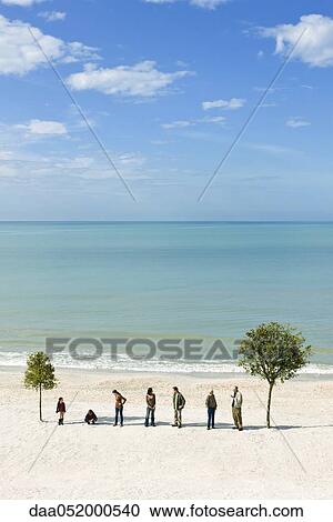 Stock Image - Group of people in row between two trees on beach. Fotosearch