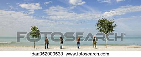 Stock Image - Group of people standing in row between two trees on beach. Fotosearch