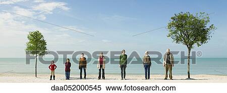 Stock Photography - Group of people standing in row between two trees on beach. Fotosearch