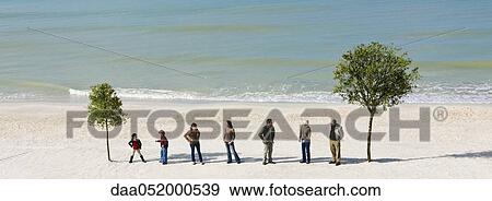 Group of people standing in row chatting between two trees on beach View Large Photo Image Stock Photo - Group of people standing in row chatting between two trees on beach. Fotosearch