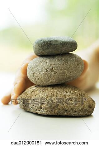 Stock Image - Hand touching stack of pebbles. Fotosearch