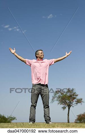 Stock Image - Happy man standing outdoors with arms raised, full length. Fotosearch