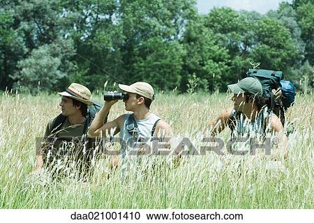 Stock Image - Hikers standing in field, one looking through binoculars. Fotosearch