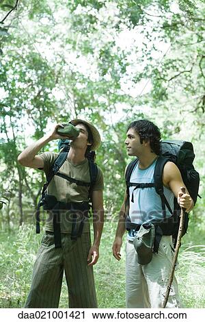 Stock Image - Hikers standing in woods, one drinking from water bottle. Fotosearch