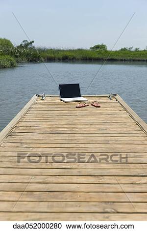 Stock Image - Laptop computer and flip-flops left on dock. Fotosearch