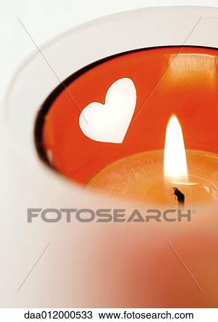 Stock Image - Lit candle in candleholder with heart pattern. Fotosearch