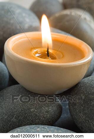 Stock Image - Lit candle on stones. Fotosearch