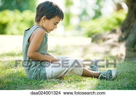 Picture - Little boy outdoors, sitting on grass, side view. Fotosearch