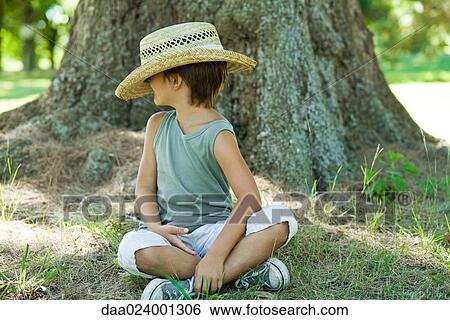 Stock Photograph - Little boy outdoors, sitting on ground with straw hat covering face. Fotosearch