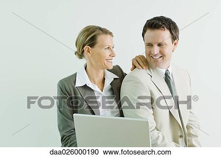 Stock Image - Male and female business associates together, smiling at each other. Fotosearch