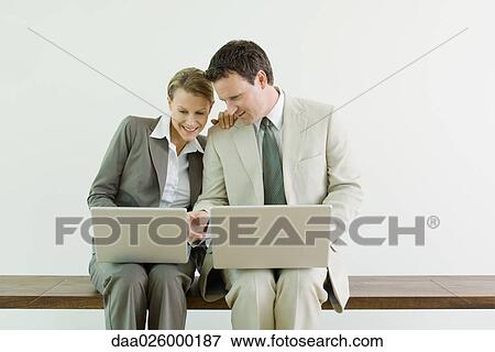 Male and female business associates sitting side by side, both using laptop computers, smiling View Large Photo Image Stock Photo - Male and female business associates sitting side by side, both using laptop computers, smiling. Fotosearch