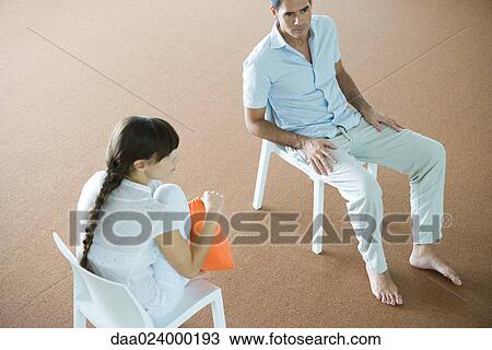 Man and woman sitting in chairs, looking away, high angle view View Large Photo Image Stock Image - Man and woman sitting in chairs, looking away, high angle view. Fotosearch