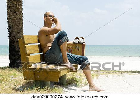 Man at the beach, sitting on bench beside suitcase, looking away View Large Photo Image Picture - Man at the beach, sitting on bench beside suitcase, looking away. Fotosearch