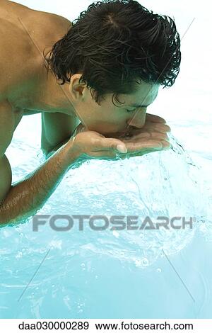 Stock Photo - Man bending over swimming pool, splashing water on face with hands, close-up. Fotosearch