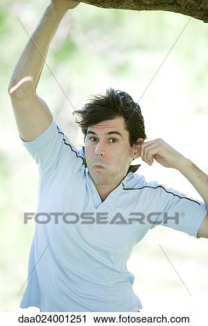 Stock Image - Man holding onto branch, pretending to be monkey. Fotosearch