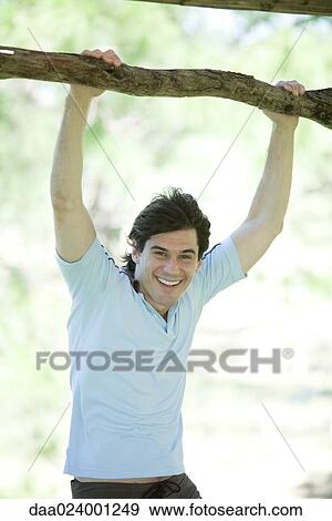 Man holding onto branch, smiling at camera View Large Photo Image Stock Photo - Man holding onto branch, smiling at camera. Fotosearch