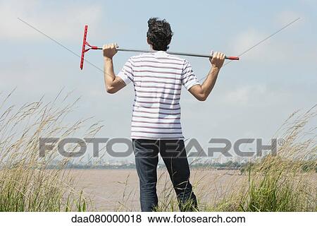 Man holding rake on shoulders, looking at city skyline from afar, rear view View Large Photo Image Stock Photo - Man holding rake on shoulders, looking at city skyline from afar, rear view. Fotosearch