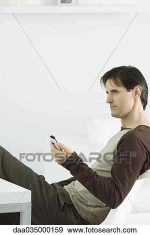 Man holding remote control, sitting and looking away View Large Photo Image Stock Photo - Man holding remote control, sitting and looking away. Fotosearch