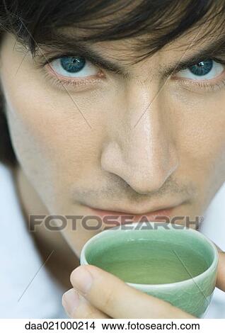 Man holding up cup of tea to mouth, looking at camera View Large Photo Image Picture - Man holding up cup of tea to mouth, looking at camera. Fotosearch