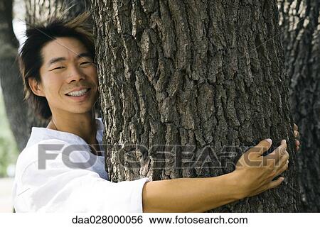 Man hugging tree trunk, smiling at camera View Large Photo Image Stock Photograph - Man hugging tree trunk, smiling at camera. Fotosearch