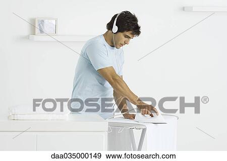 Stock Photo - Man ironing towels, listening to headphones. Fotosearch