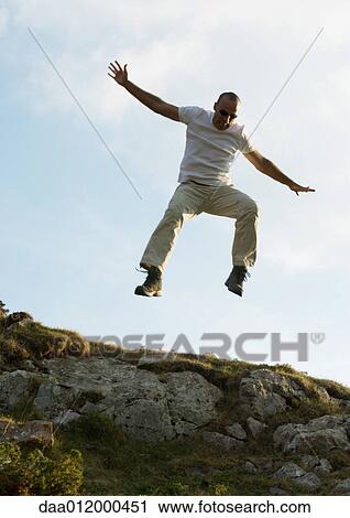 Stock Image - Man jumping in rocky landscape. Fotosearch