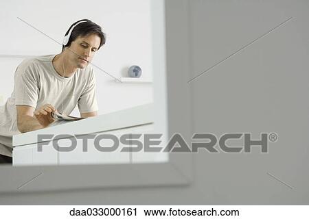 Man leaning against counter, wearing headphones and reading View Large Photo Image Stock Image - Man leaning against counter, wearing headphones and reading. Fotosearch