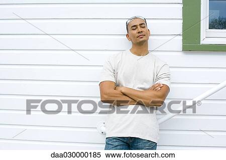 Stock Photography - Man leaning against house with arms folded. Fotosearch