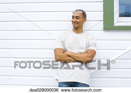 Man leaning against side of house, arms folded, smiling View Large Photo Image Stock Photograph - Man leaning against side of house, arms folded, smiling. Fotosearch